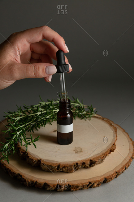 Woman pulling dropper out of an essential oil bottle surrounded by rosemary