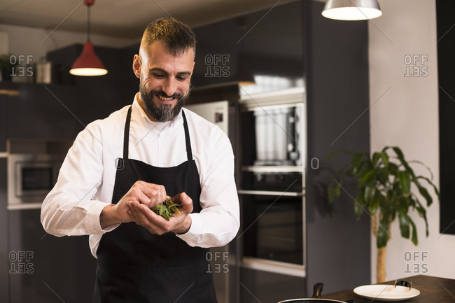 Positive chef preparing fresh herbs for dish