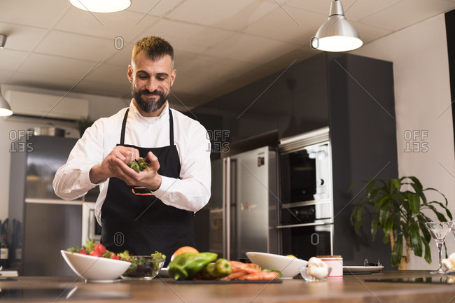 Positive chef preparing fresh herbs for dish