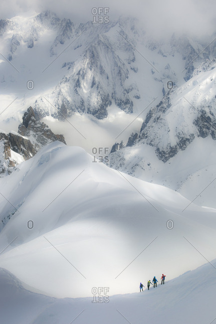A rope team of four alpinists descends a steep ridge among giant peaks