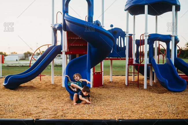 Young boy and girl sliding down slide at playground together