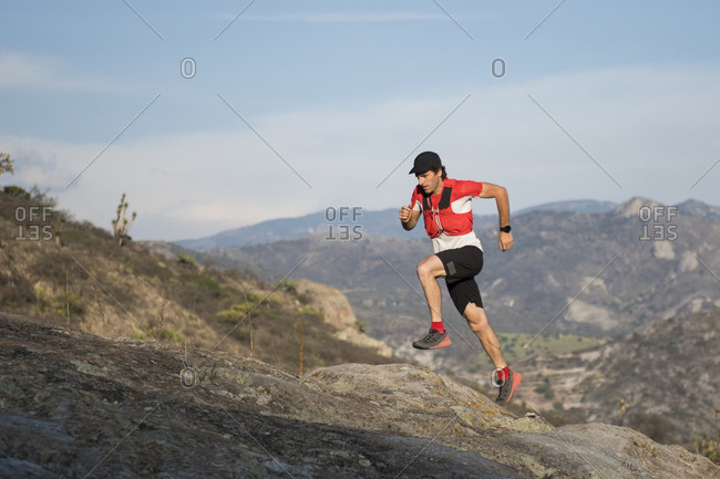 Fit, athletic middle aged man running up a rocky trail during the sunset with mountains in the background in the desertic area around el arenal, hidalgo, mexico.