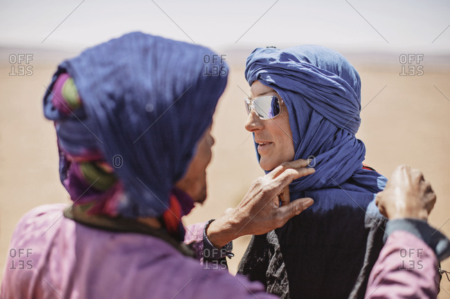 A berber tribesman ties a hijab on a caucasian female tourist, morocco