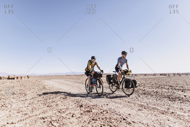 Sahara Desert, Morocco - April 8, 2019: Two smiling caucasian cyclists ride a desert dirt road in morocco