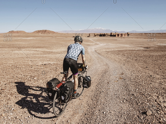 Morocco, Draa-Tafilalet, Ouarzazate - April 8, 2019: A cyclist rides through a desert toward ruins, ouarzazate, morocco