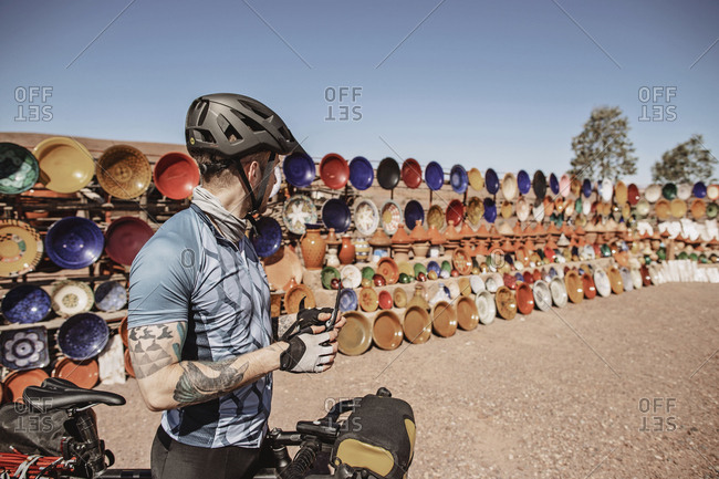 Morocco, Draa-Tafilalet, Ouarzazate - April 8, 2019: A male cyclist stops next to an outdoor ceramic market, morocco