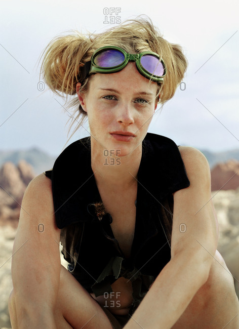 Portrait of a young woman wearing goggles on her forehead while sitting in a desert.
