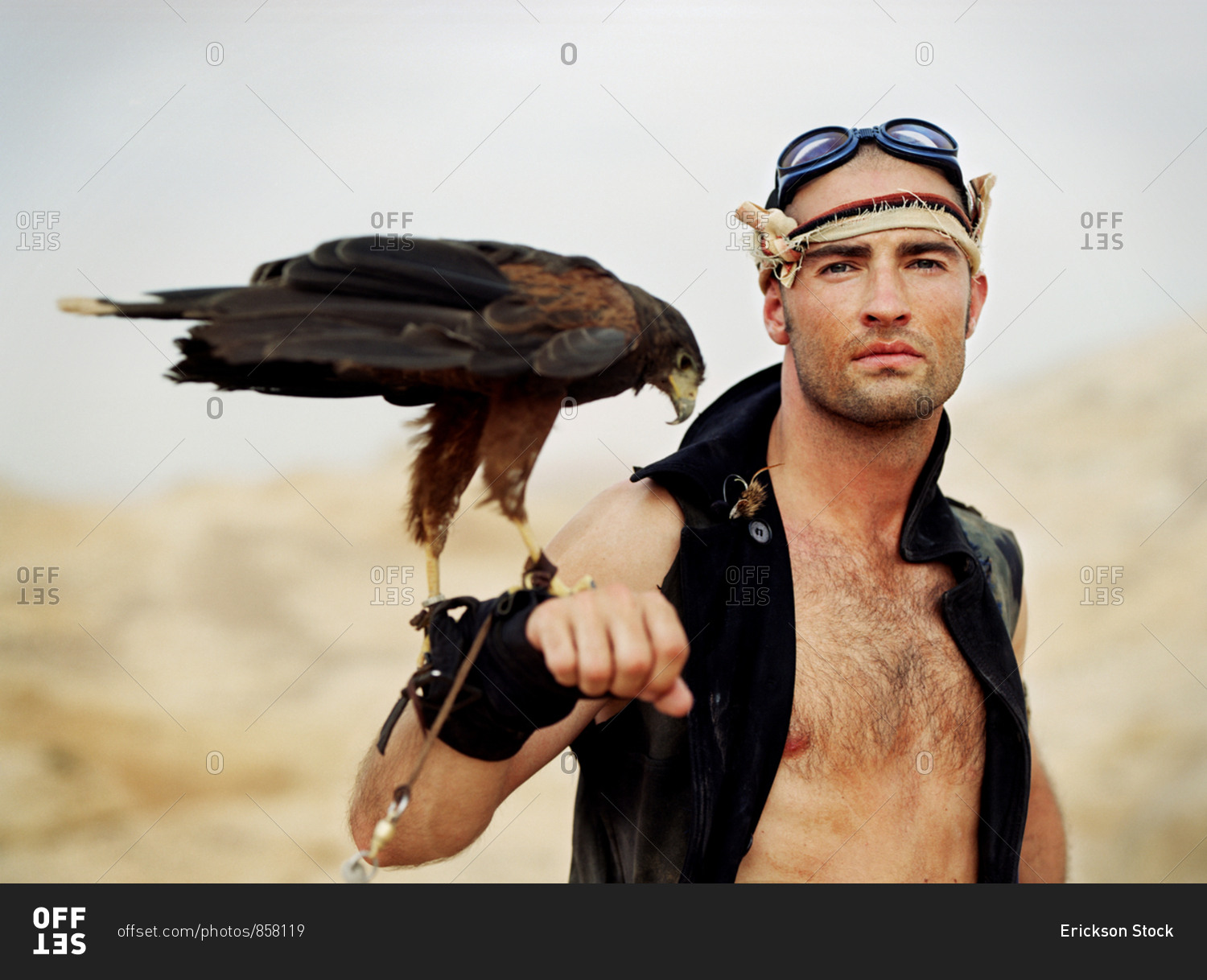 Portrait of an adventurous young man holding a bird of prey on his wrist while standing in a desert.