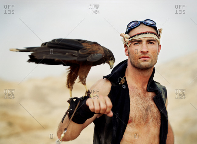Portrait of an adventurous young man holding a bird of prey on his wrist while standing in a desert.