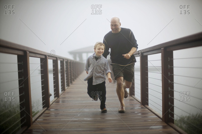 Mid-adult man having fun running along a misty pier with his young son.