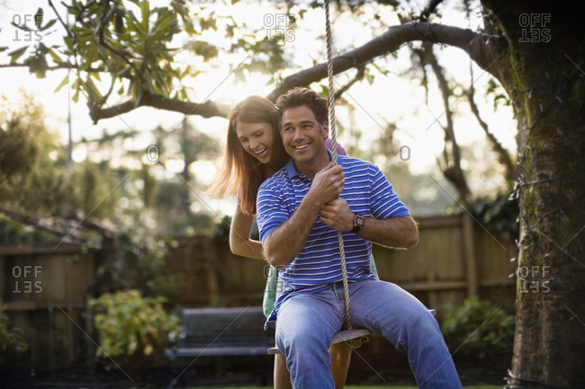 Mid-adult couple swinging on a rope in the garden.