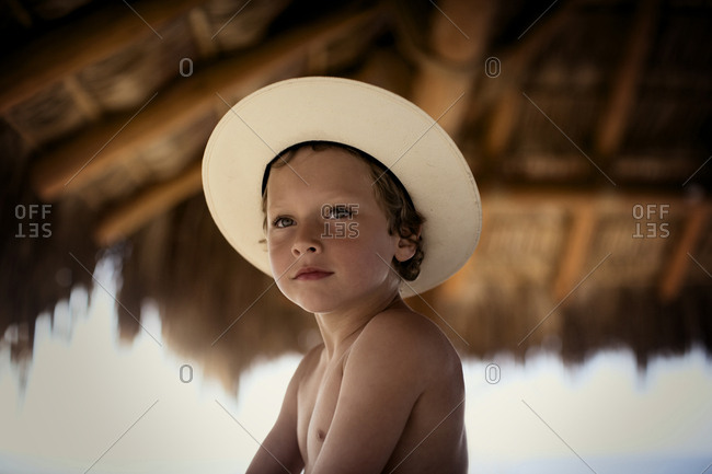 Portrait of a topless boy sitting under the thatched canopy.