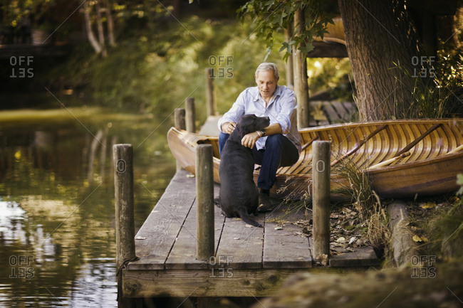 Senior adult man and his dog sitting beside a wooden canoe.