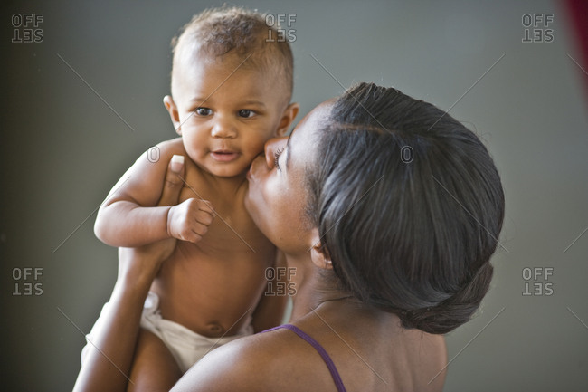 Mid-adult woman holding and kissing her newborn baby.