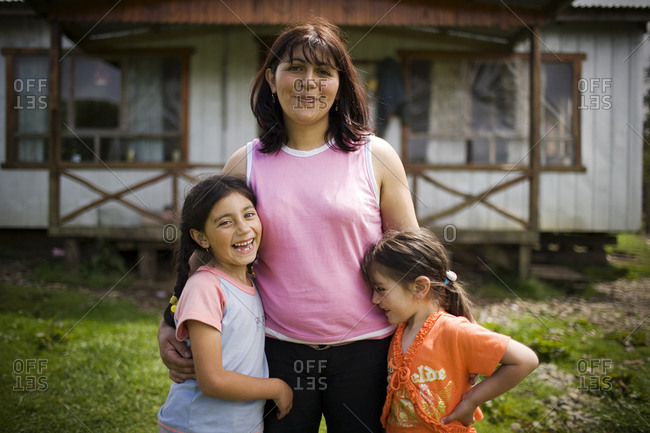 Happy mother and her two young daughters standing outside their home.