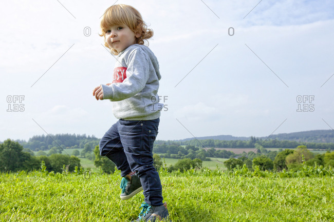 A little boy having fun on a green field in the country side, Caurel Brittany, France.