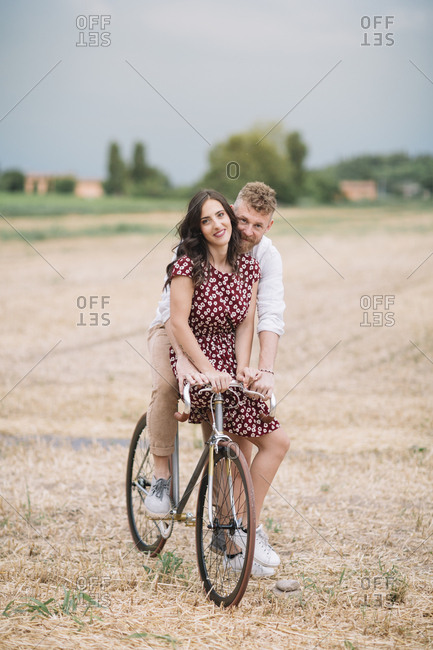 Portrait of couple on handcrafted racing cycle on stubble field