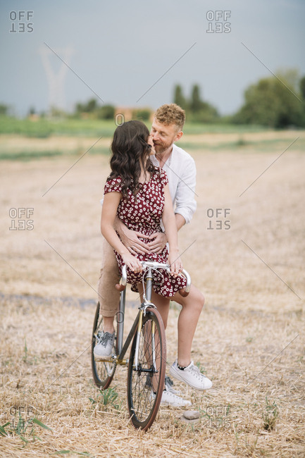 Kissing couple with handcrafted racing cycle on stubble field