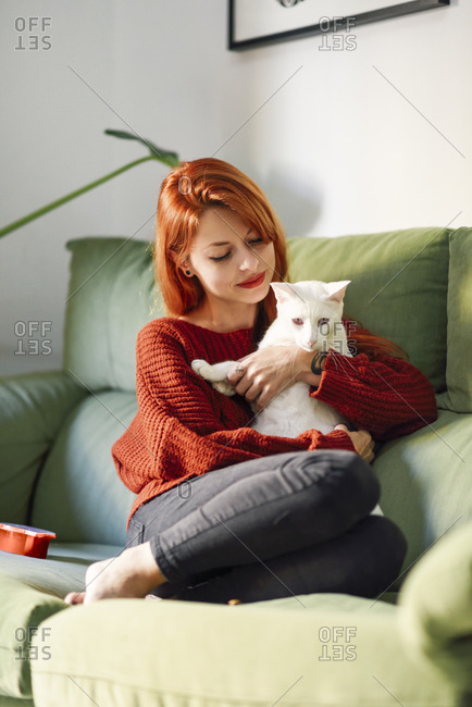Red-haired woman with cat on couch at home