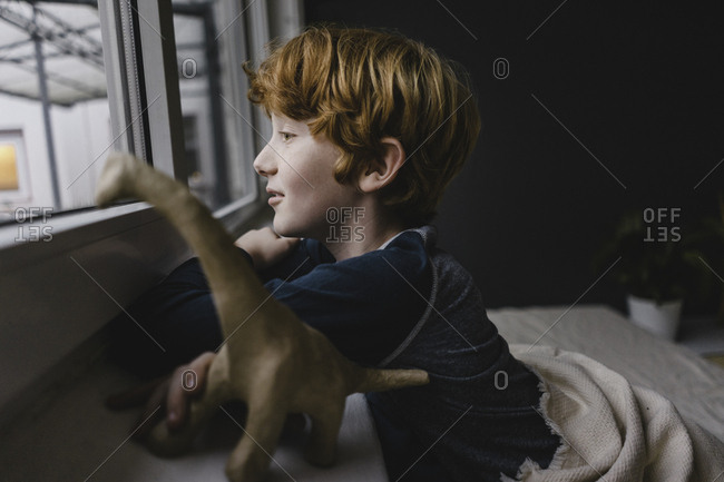 Sad boy leaning on window sill looking out of window in the evening