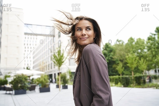Smiling businesswoman with windswept hair in the city turning round