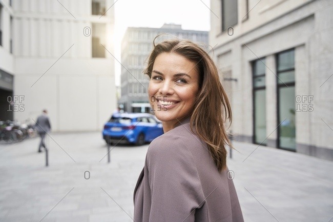 Smiling businesswoman with windswept hair in the city turning round