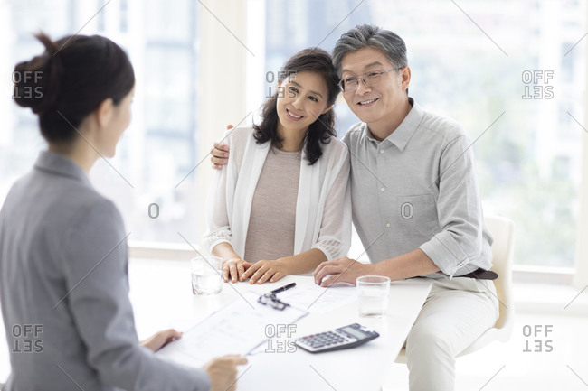 Happy mature Chinese couple talking with financial advisor at office