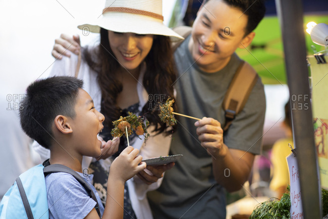 Happy young Chinese family eating snack in market