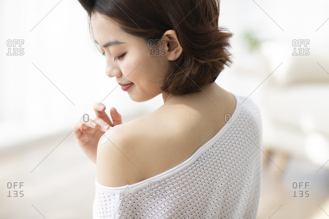 Happy young Chinese woman applying moisturizer at home