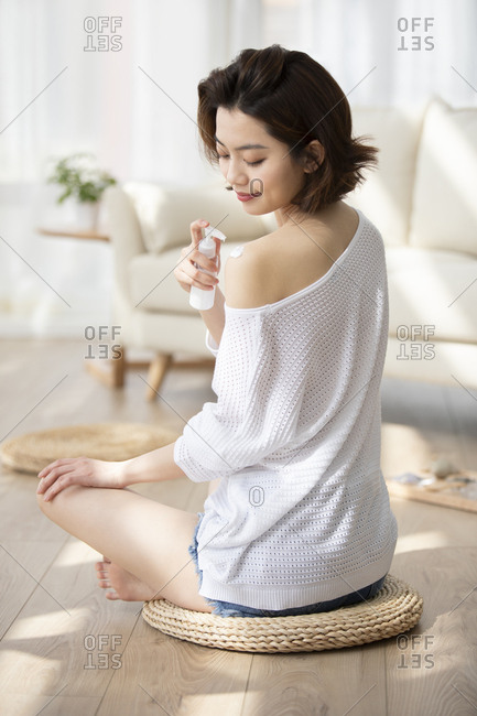 Happy young Chinese woman applying moisturizer at home