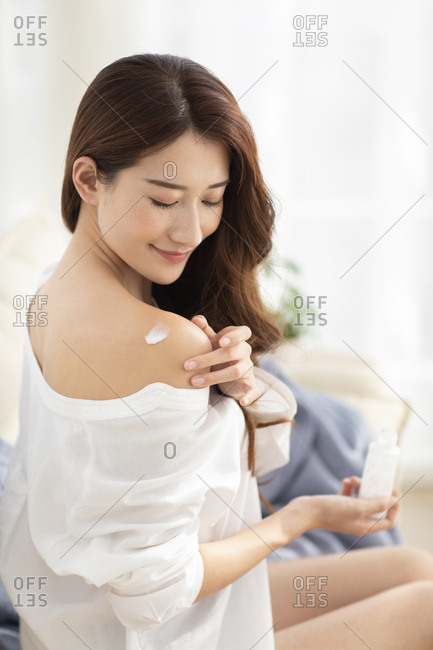 Young Chinese woman applying moisturizer at home