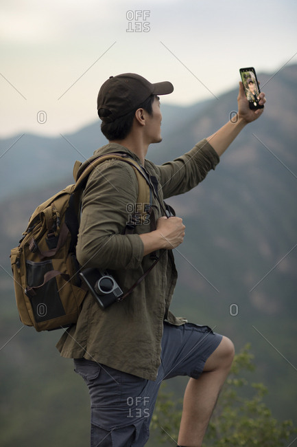 Young Chinese man taking selfie with smartphone outdoors