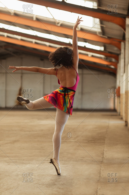 Rear view close up of a young mixed race female ballet dancer standing on one leg on her toes with arms outstretched while dancing in an empty room at an abandoned warehouse