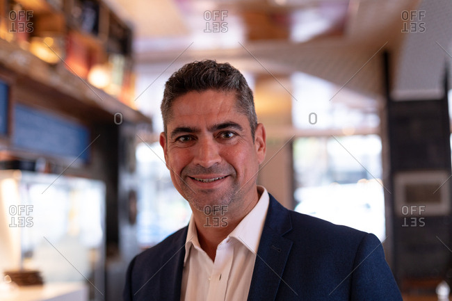 Portrait close up of a smartly dressed middle aged Caucasian male restaurant manager smiling to camera in a restaurant kitchen