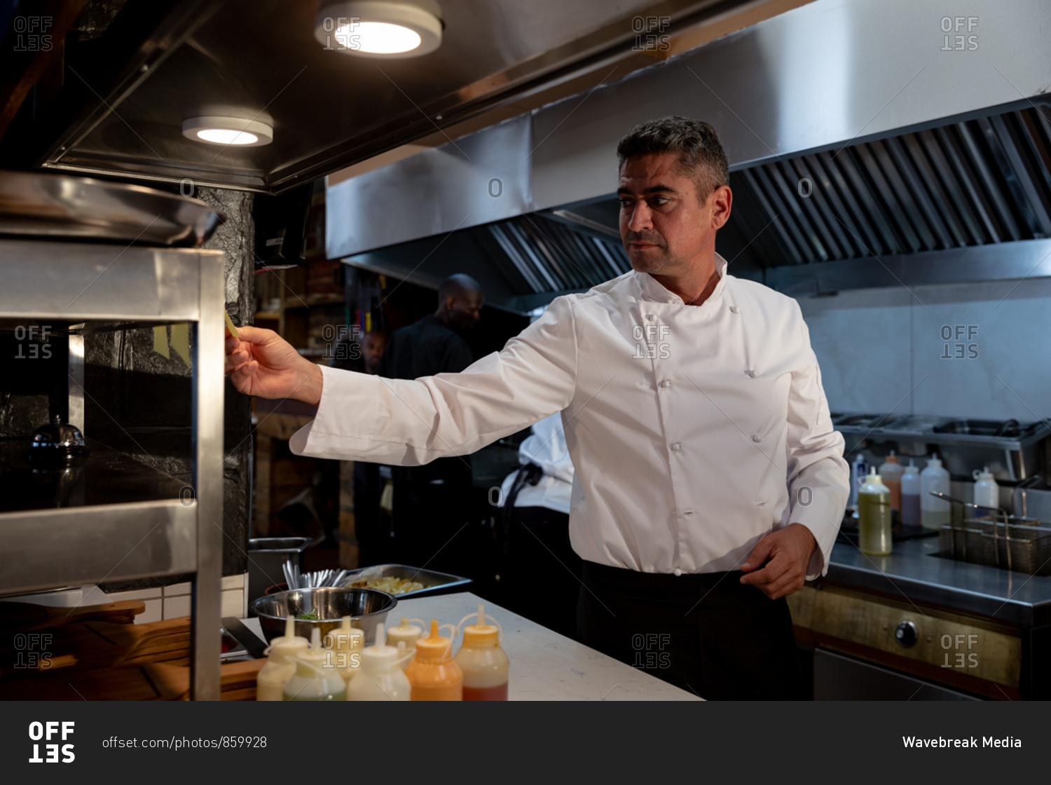 Side view close up of a middle aged Caucasian male chef checking orders at the order station in a restaurant kitchen