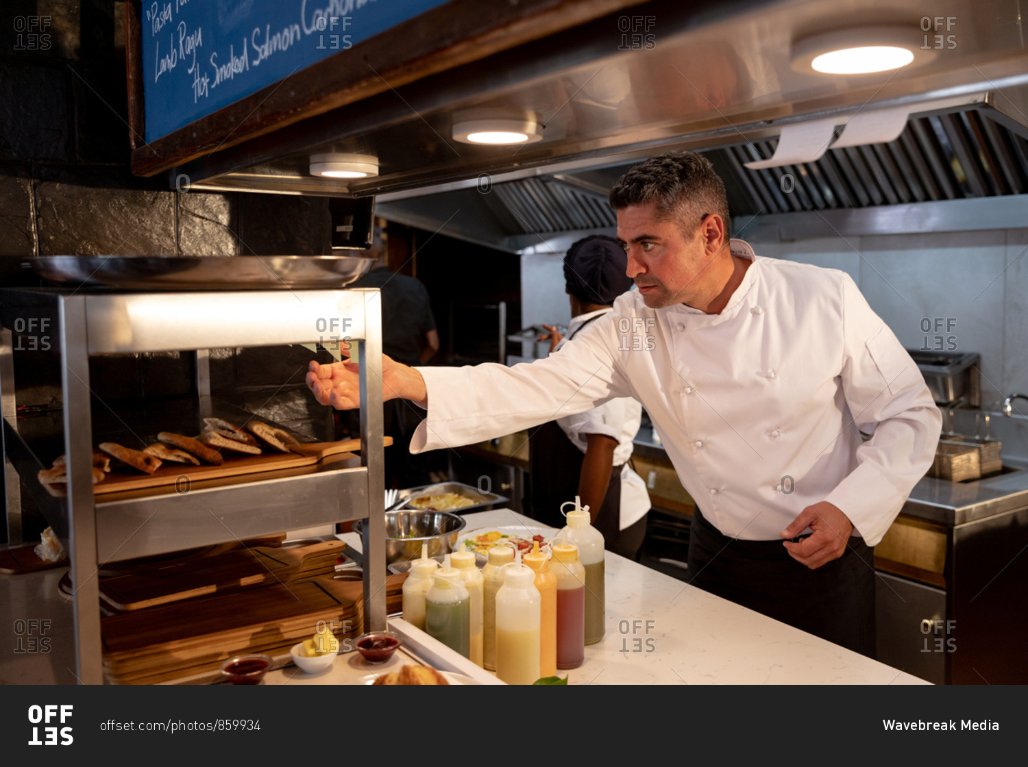 Side view close up of a middle aged Caucasian male chef checking orders at the order station in a restaurant kitchen