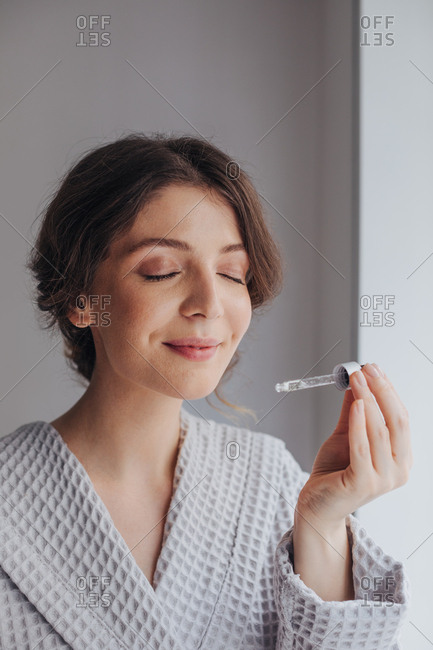 Beautiful Caucasian young woman holding cosmetic serum and smelling pipette.