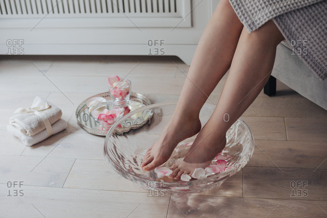 Legs of unrecognizable woman in spa bath with rose petals.
