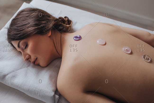 Beautiful Caucasian woman lying on massage table with crystals on her back.