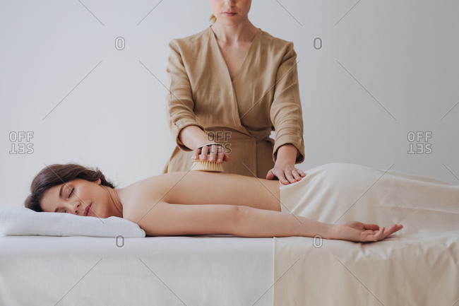 Pretty Caucasian woman enjoying brush massage at spa salon.
