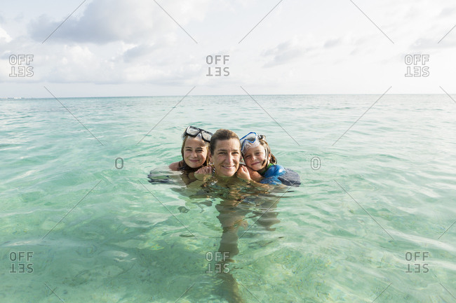 Adult woman standing in ocean water at sunset with her children