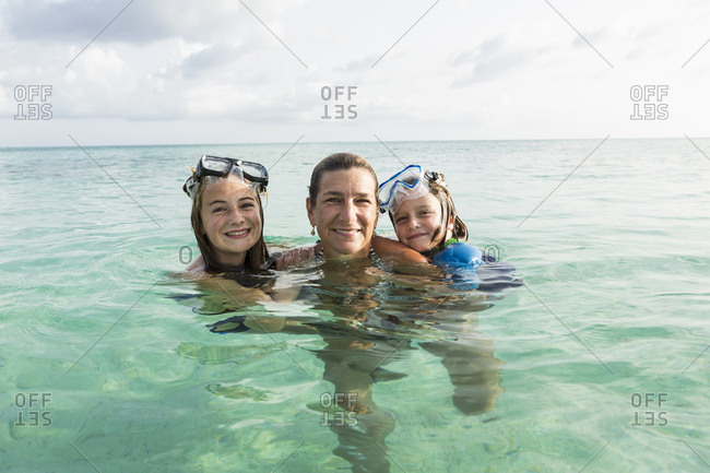 Adult woman standing in ocean water at sunset with her children