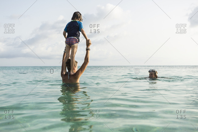 5 year old son on mother's shoulders leaping into the ocean at sunset