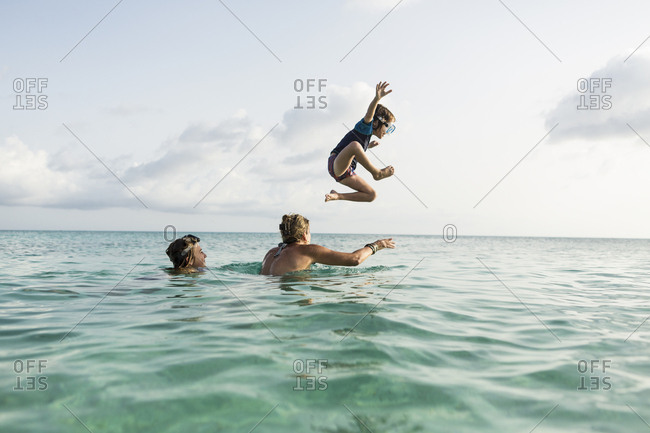 5 year old son on mother's shoulders leaping into the ocean at sunset