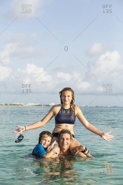 Adult woman standing in ocean water at sunset with her children