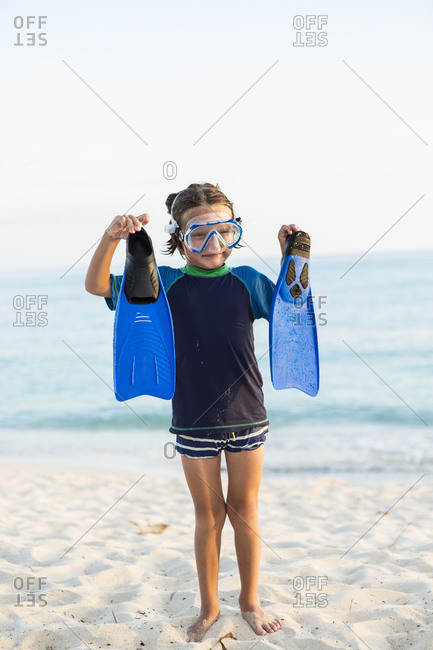A young boy wearing a snorkel mash and holding up his blue flippers.