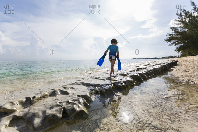 5 year old boy walking on rocks on the shore with swimming fins