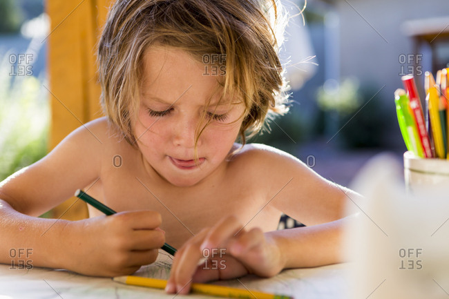 Shirtless 5 year old boy drawing with colored pencils