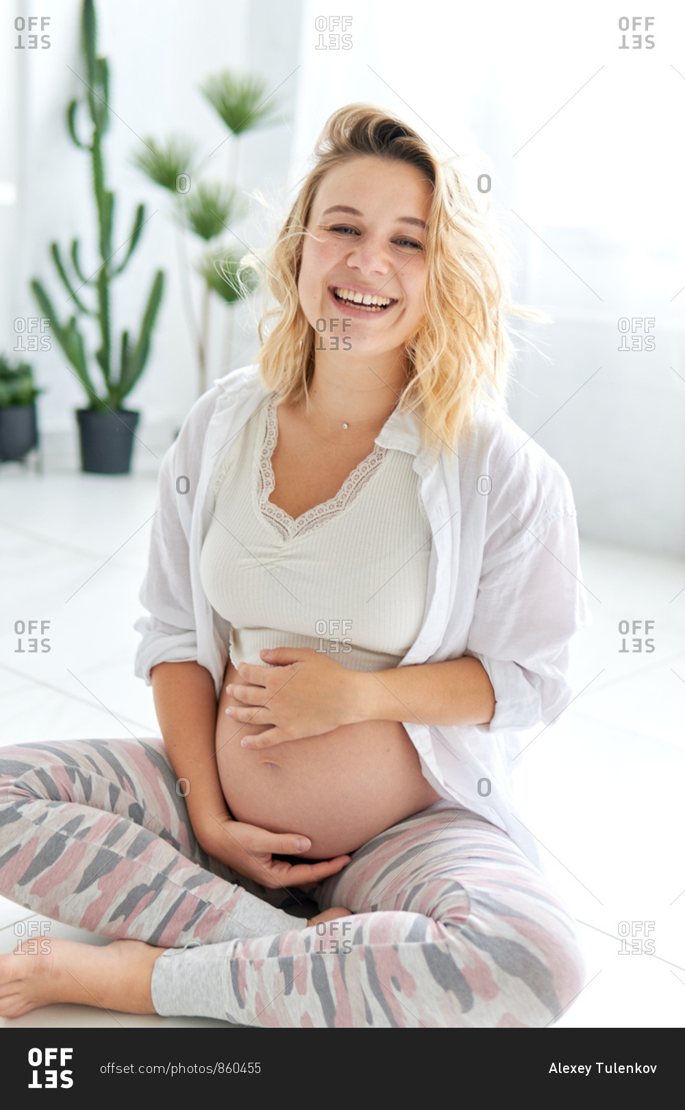 Smiling Pregnant Woman Sitting On Tile Floor Touching Her Belly Stock