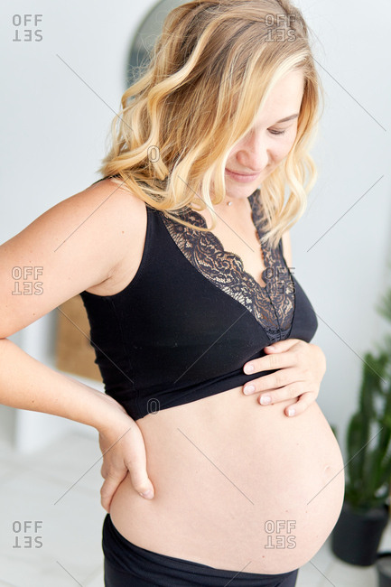 Beautiful pregnant woman dressed in black looking down and touching her  bare belly stock photo - OFFSET